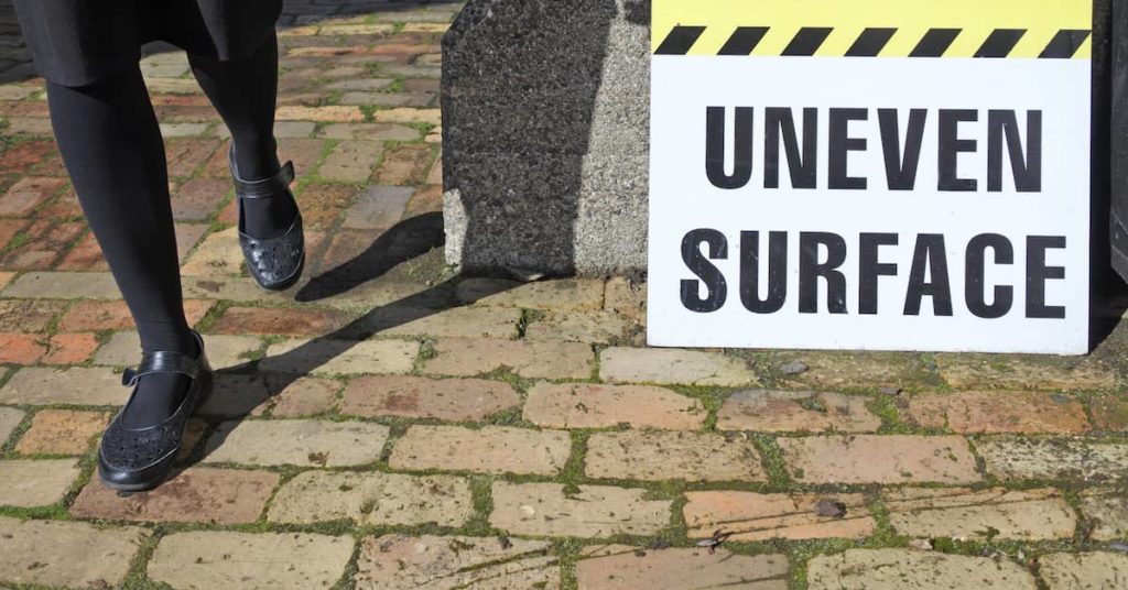 woman walking near "Uneven Surface" warning sign