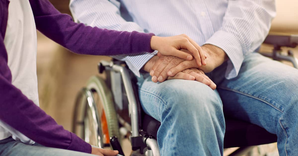 caregiver holding the hand of an elderly man in a wheelchair